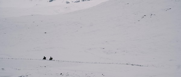 Two distant horse riders in snowfall